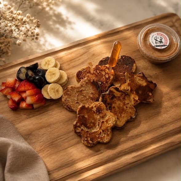 Dog pancakes on a wooden board with strawberries, banana and blueberries, honey and a pot of peanut butter