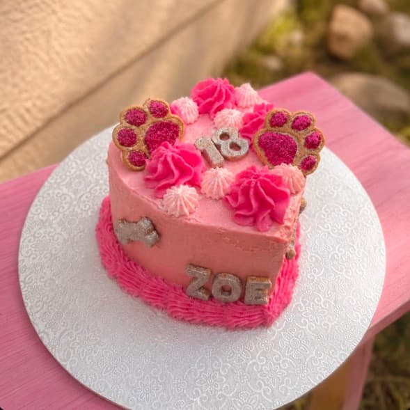 A small classic heart-shaped birthday cake in pink, with paw prints, the dog's name and age